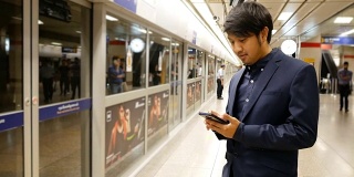亚洲商人在火车站等车时用智能手机发短信