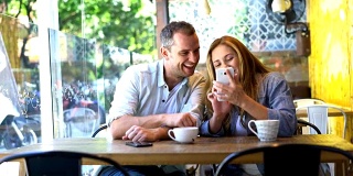 一对幸福的情侣在自助餐厅喝咖啡，在智能手机上看照片