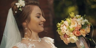 年轻美丽的新娘带着婚礼花束，微笑着待在古老的石墙附近