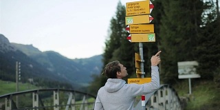 男子退后在旅游路标选择指向目的地的自然近距离慢动作。在瑞士或德国的旅行者在决定去哪里时，会显示乡村地名