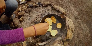 手用勺子在煎锅里翻动油饼，从上面打开火，烟雾上升到镜头，准备食物徒步