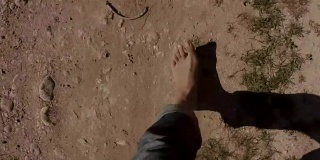 POV女士双腿不穿鞋，穿着牛仔裤走在荒芜的土地上，以第一人称视角，赤着脚，石头和沙子