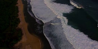 无人机拍摄的日落时分海浪冲破海岸的画面。印尼巴厘岛