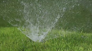 阳光明媚的日子里，草坪自动浇水系统洒水喷头的一个喷头的一个喷头的特写，慢动作视频素材模板下载