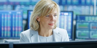 肖像的高级女性股票交易员在她的工作站操作。在她的多个显示器显示数据，股票号码和图表。
