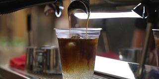 特写新鲜冰咖啡，冷咖啡与冰块在一次性透明杯简单地倒在冰。意大利浓缩咖啡机。咖啡文化和专业的咖啡制作、咖啡送走、服务、餐饮理念