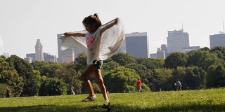 曼哈顿中央公园。以摩天大楼为背景的草地景观。一个小女孩拿着大手帕转来转去玩