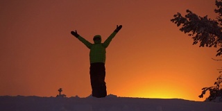 日出时分，一个徒步旅行者向橘黄色的天空掷雪，骄傲地伸出双臂
