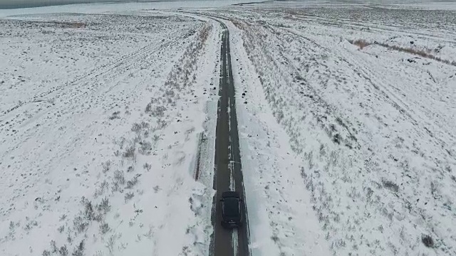 一辆黑色汽车行驶在雪地里的乡村道路上，无人机拍摄的鸟瞰图