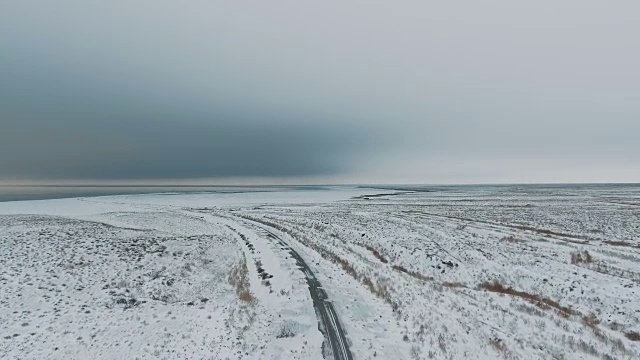 一辆黑色汽车行驶在雪地里的乡村道路上，无人机拍摄的鸟瞰图