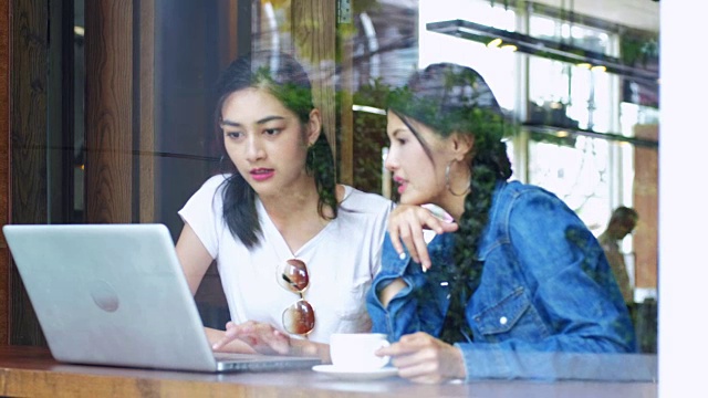 两个女朋友在咖啡馆用笔记本电脑分享咖啡。