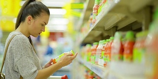 近距离肖像吸引年轻女孩选择果汁在超市附近的货架