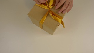 近上俯视图高角度。男人的手做蝴蝶结缎带在棕色纸盒礼盒。白色米色背景。为庆祝节日准备礼物。圣诞礼物盒子。视频素材模板下载