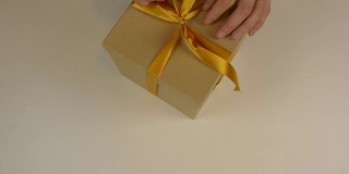 近上俯视图高角度。男人的手做蝴蝶结缎带在棕色纸盒礼盒。白色米色背景。为庆祝节日准备礼物。圣诞礼物盒子。