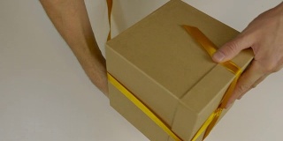 准备礼物送礼物。礼盒包装与金丝带。用手用黄丝带将礼盒包起来，打一个蝴蝶结。近上俯视图高角度。