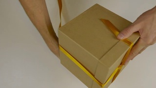 准备礼物送礼物。礼盒包装与金丝带。用手用黄丝带将礼盒包起来，打一个蝴蝶结。近上俯视图高角度。视频素材模板下载