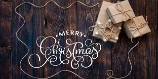 手写白色圣诞快乐动画书法文字在深色木质背景与礼物和节日装饰。视频贺卡。快乐的感觉