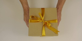 手上伸着一个礼盒，用金色的丝带系着一个蝴蝶结。送礼物。手捧礼盒祝贺某人的节日。赠送礼物。纸板箱是灰棕色的。