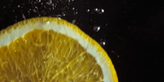 超近镜头。宏观的观点。切片多汁的新鲜橙子落入水中的慢镜头。黑色背景上的气泡