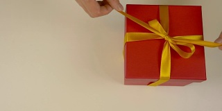 大的拆开红色礼品盒与金色丝带。用手解开红色礼品盒上金色丝带的丝带。俯视图高角度。关闭了。