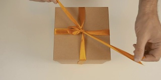 用手解开红色礼品盒上金色丝带的丝带。俯视图高角度。关闭了。打开带有金色丝带的棕色礼盒。打开礼盒礼物。