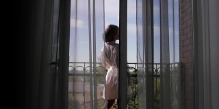一个年轻女子走近窗户，打开阳台，欣赏。清晨新娘等待婚礼