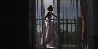 一个年轻女子走近窗户，打开阳台，欣赏。清晨新娘等待婚礼