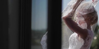 美丽的新娘在窗户附近的面纱摆姿势。慢动作