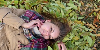一个穿着大衣的年轻女子躺在秋叶上。微笑的幸福