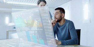 在不久的将来，男性和女性办公室工作人员讨论在透明电脑显示器上显示的图形统计。漂亮的人说话。屏幕上的交互式图表。