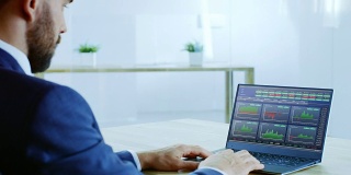 在肩膀上的成功商人在笔记本电脑上工作，屏幕显示股票市场股票行情信息。市场的兴衰。办公室是明亮和现代的。