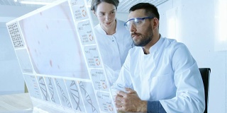 在未来的实验室里，男科学家和女科学家一边在透明显示计算机上工作一边交谈。屏幕显示人类DNA序列。