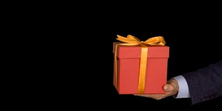 一个穿着西装的男人手里拿着一个红色礼品盒，上面有一个金色的蝴蝶结。手与礼物出现在相框中。红色的礼盒。商人送礼物。Alpha通道色度键透明背景。