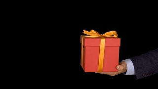 一个穿着西装的男人手里拿着一个红色礼品盒，上面有一个金色的蝴蝶结。手与礼物出现在相框中。红色的礼盒。商人送礼物。Alpha通道色度键透明背景。视频素材模板下载
