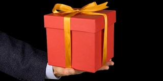 一个穿着西装的男人手里拿着一个红色礼品盒，上面有一个金色的蝴蝶结。手与礼物出现在相框中。红色的礼盒。商人送礼物。Alpha通道色度键透明背景。