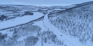 在冬天的早晨，一辆汽车在雪山脚下的高速公路上行驶