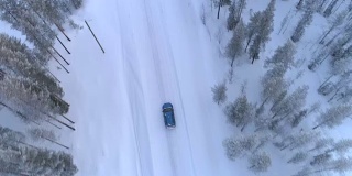 空中俯瞰:汽车行驶在积雪的道路上，穿过寒冷的冬季云杉森林