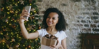 Curly十几岁的女孩在圣诞树附近用智能手机摄像头在线聊天