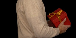一名身穿米色毛衣的白人男子手里拿着一个礼品盒。侧视图的男人在休闲米色毛衣。人类给了礼物。Alpha通道色度键透明背景。锁定。