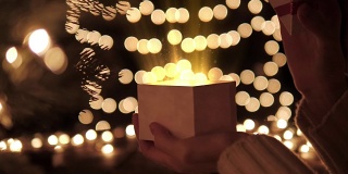 女人打开白色的圣诞礼盒与光芒的魔术灯散景灯的背景