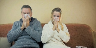 慢镜头:一个男孩和一个女孩坐在家里的沙发上打喷嚏，用手帕擦鼻涕。