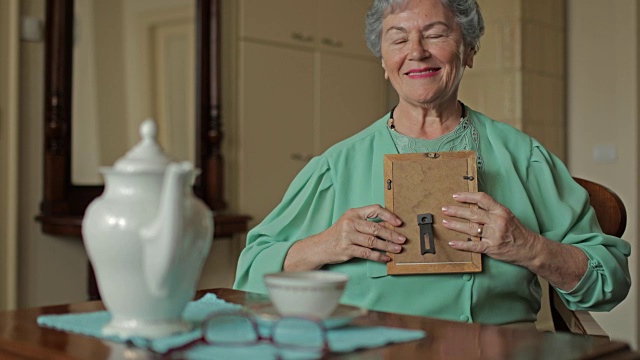 一个怀旧的老妇人在家看着相框里的照片。
