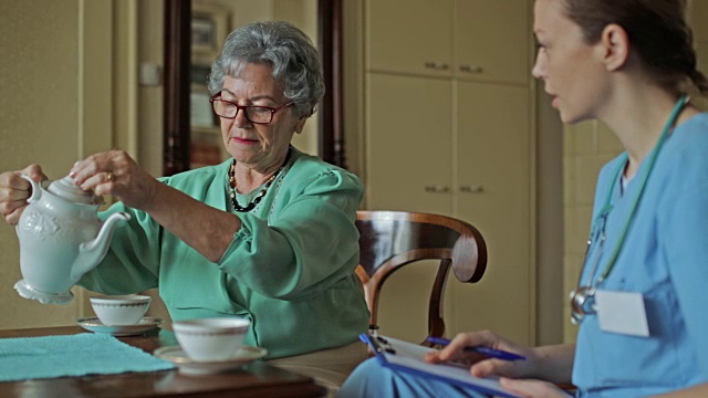 年长的妇女和家庭看护聊天，在家喝茶。