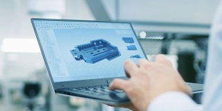特写的工程师持有笔记本电脑与CAD组件模型在屏幕上。背景中的现代工厂设备。