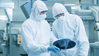 两名身穿无菌服的工程师/科学家/技术员手持将被制造成计算机芯片的半导体硅片。他们在一家现代半导体制造工厂工作。视频素材模板下载