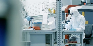 两名身穿无菌服的工程师/科学家/技术员使用显微镜进行研究。他们在一家电子元件制造厂工作。