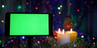 绿色屏幕的智能手机。在新年的背景下，闪烁的花环，燃烧的蜡烛。