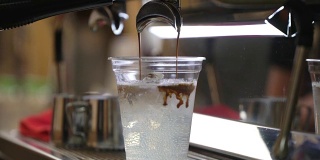 特写新鲜冰咖啡，冷咖啡与冰块在一次性透明杯简单地倒在冰。意大利浓缩咖啡机。咖啡文化和专业的咖啡制作、咖啡送走、服务、餐饮理念。间隔拍摄