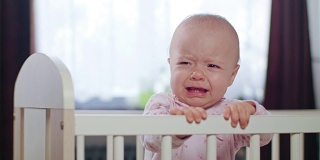 婴儿站在家里的婴儿床里。哭