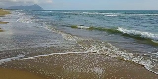 泡沫图案在沙滩的海浪和山的背景。航空摄影测量。慢动作